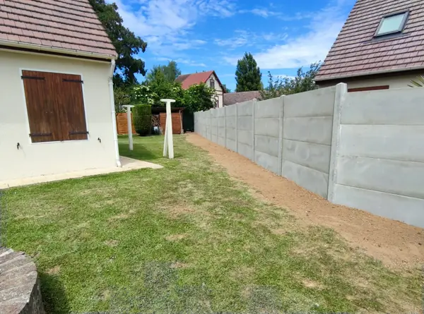 Clôture en plaques de béton posée en limite de jardin.